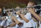 Male student with friends blow the trumpet with the band for performance on stage at night.