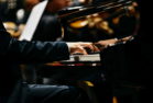 Pianist playing a piece on a grand piano at a concert, seen from the side.